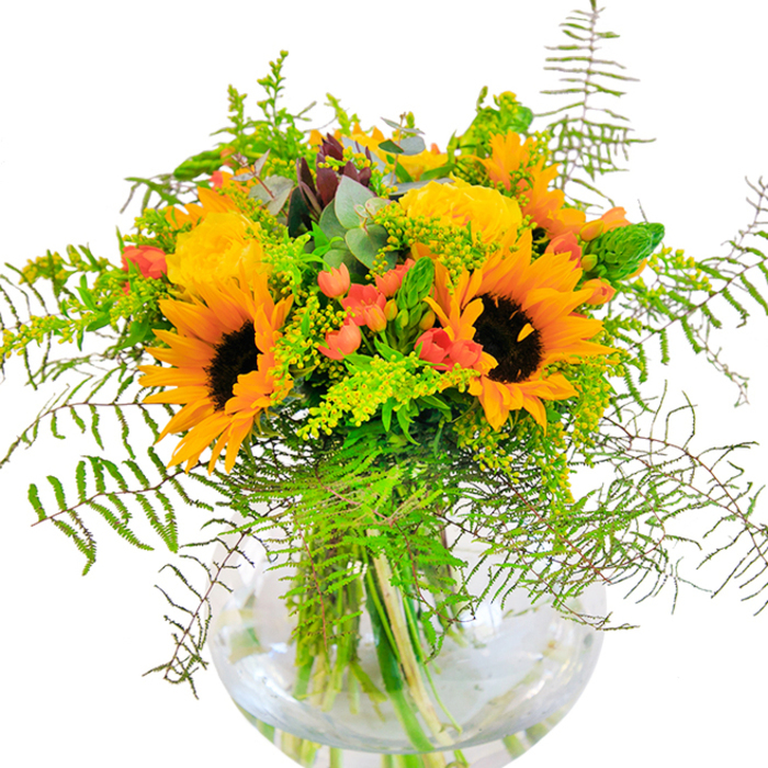 This sun-drenched bouquet, inspired by the tranquil beauty of Chalfont St Giles, exudes pure exuberance and optimism. Centered around lavish sunflowers-each with a velvety espresso-brown core and luminous golden petals-the arrangement is completed with elegant yellow garden roses unfurling in soft, spiraling layers. Glossy clusters of red hypericum berries nestle among a diversity of lush green foliage, their jewel tones standing out against the matte simplicity of the petals, much like poppies scattered in village meadows. Airy fern fronds, solidago sprigs studded with tiny yellow blossoms, and slender flower spikes add texture and movement, reminiscent of walks through the leafy paths that wind around the River Misbourne. Eucalyptus leaves, cool and blue-green, lend a whisper of woodland freshness. Presented in a crystal-clear, rounded vase, the bouquet's stems are visible through the water, giving the entire piece a refreshing brightness. Illuminated by soft, ambient light, the bouquet's details come to life: the suede texture of sunflower petals, the delicate spirals of the rose, the crisp snap of fresh foliage. This arrangement, expertly crafted by local florists, is perfect for marking happy occasions-be it a celebratory gathering, a birthday, or to simply bring the warmth of Chalfont St Giles indoors.